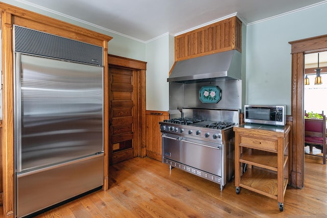 kitchen featuring premium appliances, ornamental molding, wainscoting, light wood-type flooring, and range hood