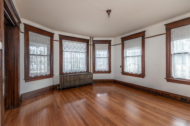 spare room with wood-type flooring, baseboards, crown molding, and radiator heating unit