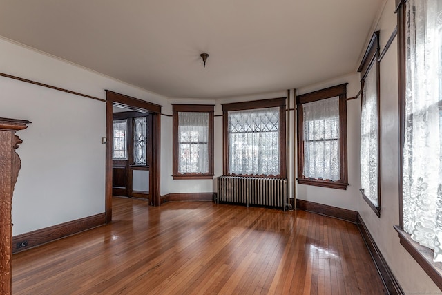 unfurnished room with radiator, wood-type flooring, baseboards, and crown molding