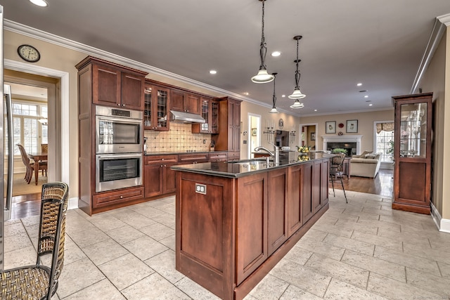 kitchen with sink, decorative light fixtures, an island with sink, stainless steel double oven, and decorative backsplash