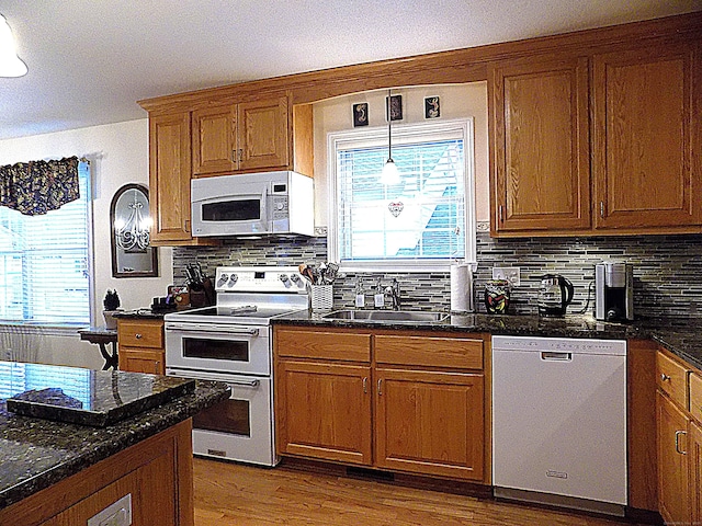 kitchen with white appliances, light wood-type flooring, dark stone counters, pendant lighting, and sink