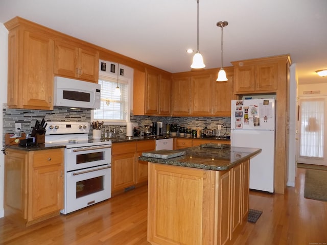 kitchen with decorative light fixtures, dark stone countertops, a center island, white appliances, and light hardwood / wood-style flooring