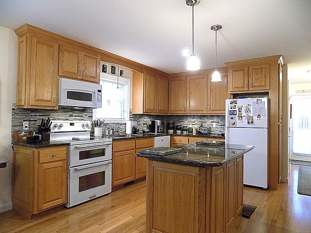 kitchen with white appliances, light wood-type flooring, dark stone countertops, pendant lighting, and a center island