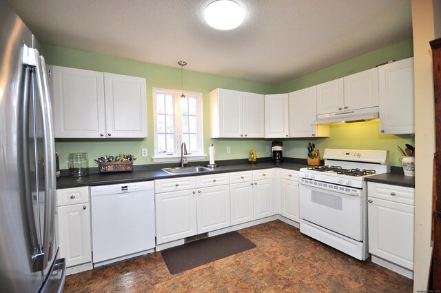 kitchen with dark countertops, white cabinetry, a sink, white appliances, and under cabinet range hood