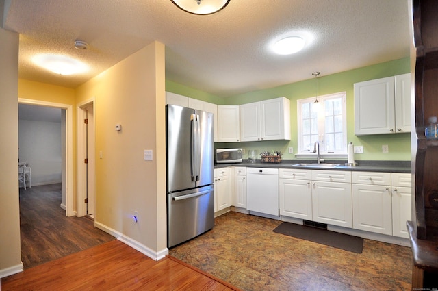 kitchen with freestanding refrigerator, dishwasher, dark countertops, and a sink