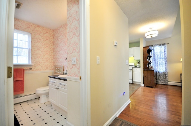 bathroom with toilet, vanity, baseboard heating, and wallpapered walls