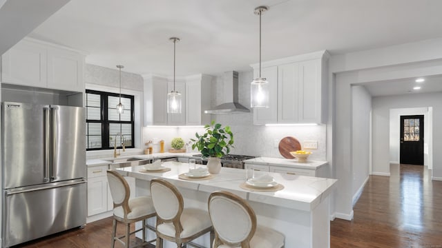 kitchen featuring wall chimney range hood, sink, high quality fridge, white cabinets, and a kitchen island