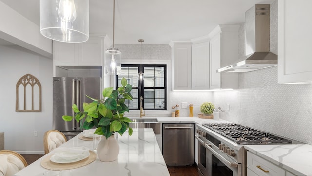 kitchen featuring wall chimney range hood, premium appliances, light stone countertops, white cabinets, and decorative light fixtures