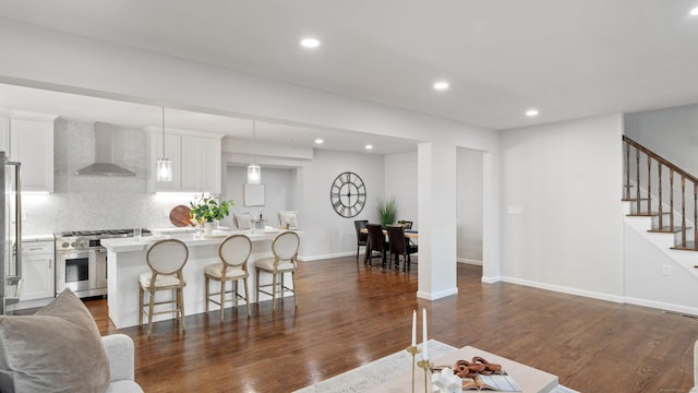 kitchen with a kitchen island, white cabinets, hanging light fixtures, stainless steel appliances, and wall chimney exhaust hood