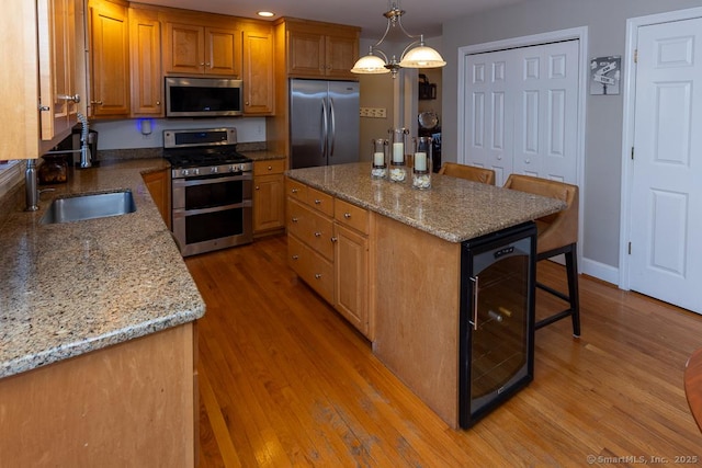 kitchen featuring beverage cooler, a kitchen island, appliances with stainless steel finishes, decorative light fixtures, and a sink