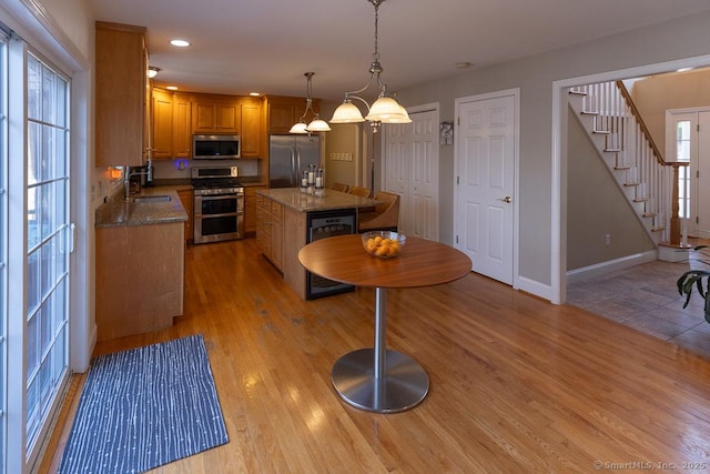 kitchen featuring light wood finished floors, beverage cooler, appliances with stainless steel finishes, a center island, and hanging light fixtures