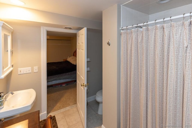 ensuite bathroom with toilet, ensuite bathroom, curtained shower, tile patterned flooring, and a sink