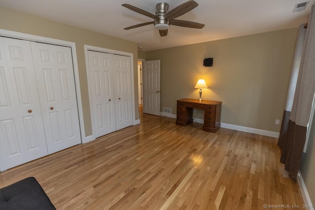 unfurnished bedroom featuring baseboards, light wood finished floors, visible vents, and multiple closets