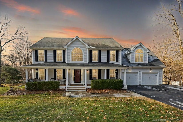 colonial inspired home featuring driveway, a garage, a porch, and a front yard