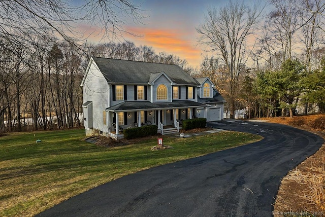 view of front facade with driveway, covered porch, a garage, and a front lawn