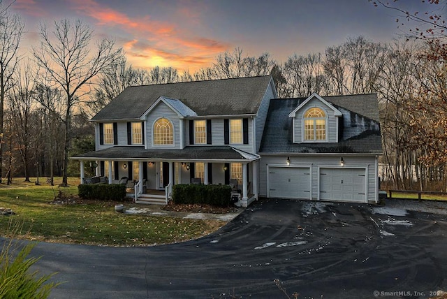 view of front of home with aphalt driveway, covered porch, a front lawn, and a garage