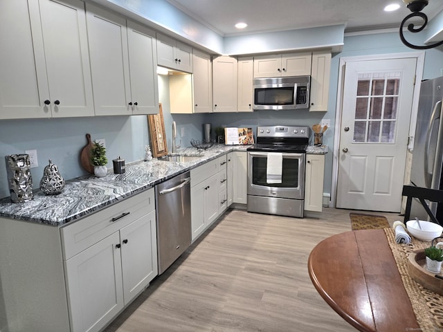 kitchen with sink, ornamental molding, appliances with stainless steel finishes, light stone countertops, and light hardwood / wood-style floors