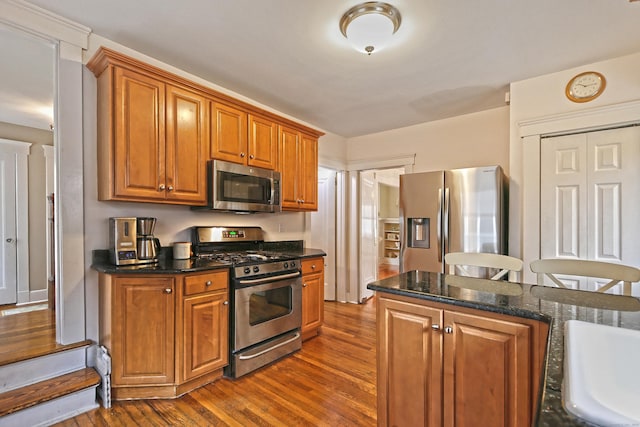 kitchen featuring appliances with stainless steel finishes, a kitchen bar, dark hardwood / wood-style floors, and dark stone counters