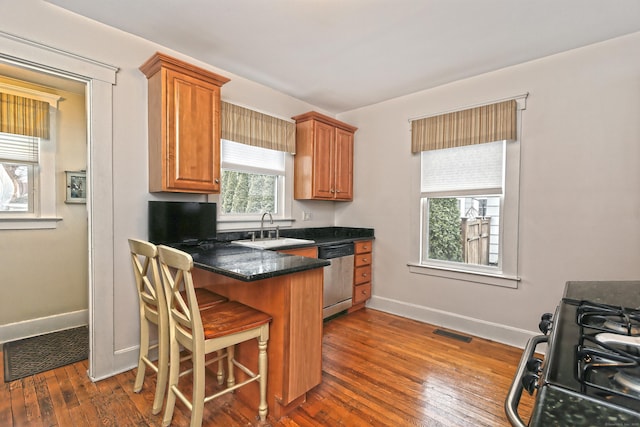 kitchen with dishwasher, sink, gas range oven, a breakfast bar area, and dark hardwood / wood-style flooring