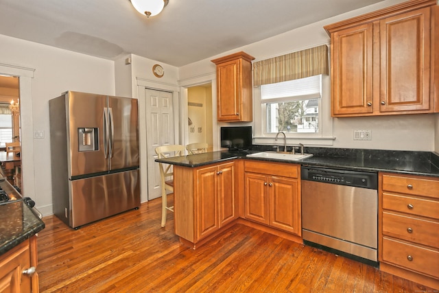 kitchen featuring kitchen peninsula, appliances with stainless steel finishes, sink, and dark stone counters