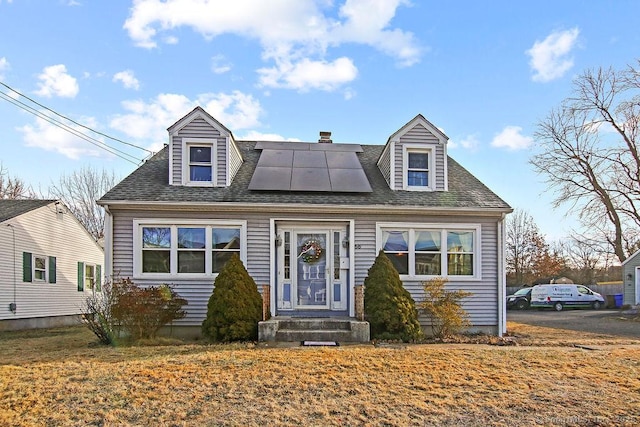 cape cod house with a front yard and solar panels