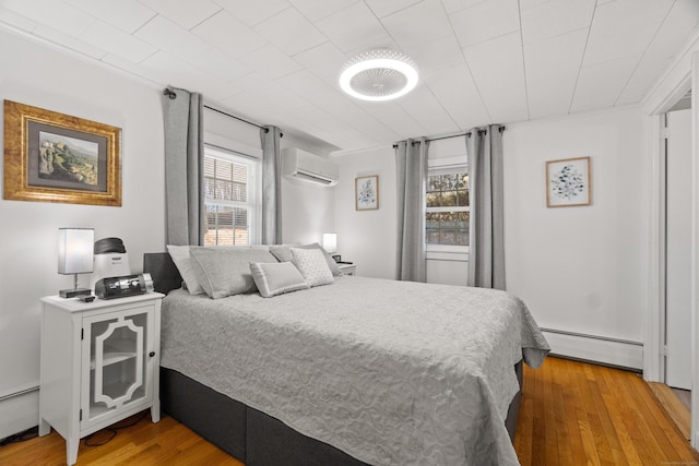 bedroom featuring light wood-style flooring, multiple windows, baseboard heating, and a wall mounted air conditioner