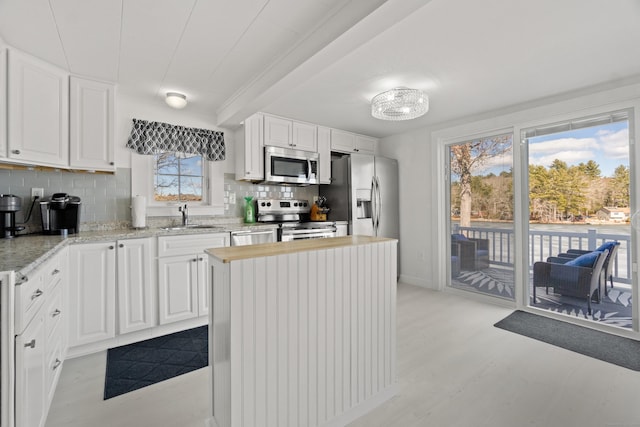 kitchen with white cabinets, light wood-style flooring, a sink, stainless steel appliances, and backsplash