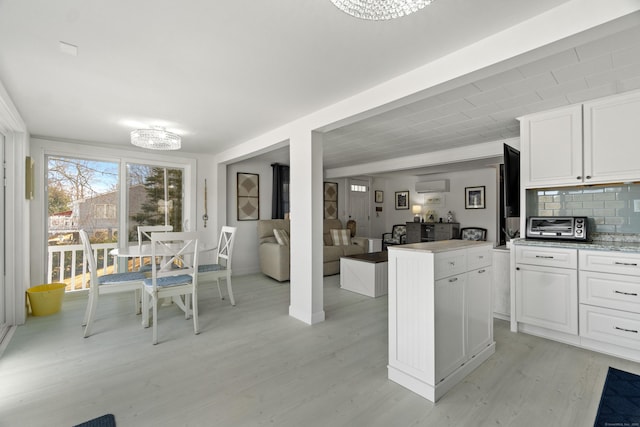 kitchen featuring a wall unit AC, light wood finished floors, white cabinetry, and decorative backsplash