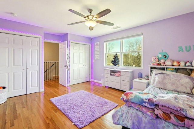 bedroom with ceiling fan, light wood-type flooring, and multiple closets