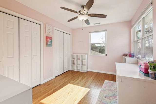 bedroom with ceiling fan, two closets, and light hardwood / wood-style flooring