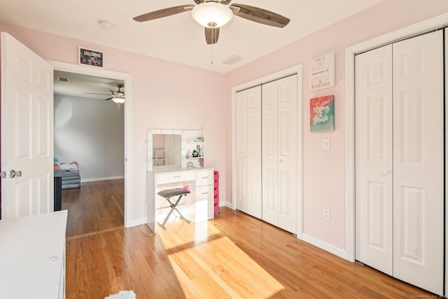 bedroom with ceiling fan, two closets, and wood-type flooring