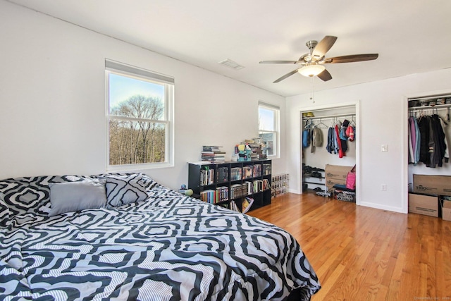 bedroom with ceiling fan, hardwood / wood-style flooring, multiple closets, and multiple windows