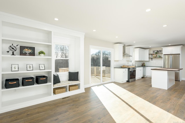 kitchen with appliances with stainless steel finishes, white cabinetry, dark hardwood / wood-style flooring, a center island, and wall chimney exhaust hood