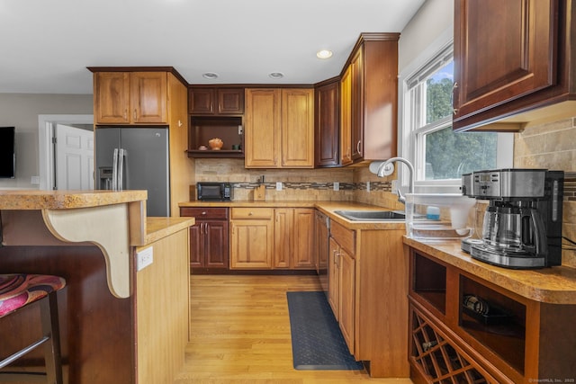 kitchen featuring stainless steel fridge with ice dispenser, a breakfast bar area, decorative backsplash, light hardwood / wood-style flooring, and sink