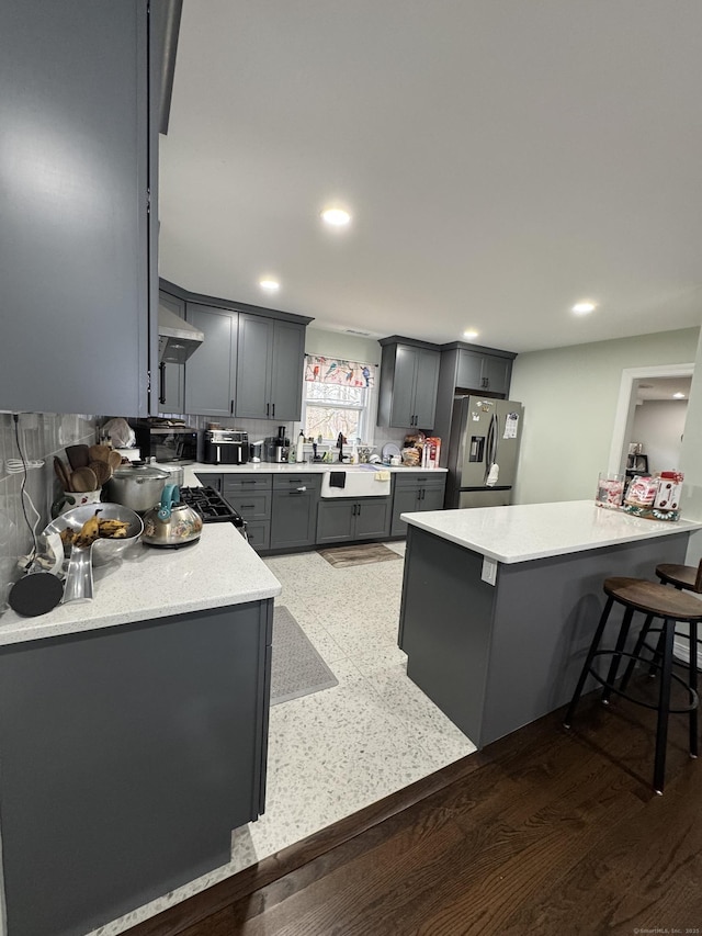 kitchen featuring sink, stainless steel fridge, kitchen peninsula, gray cabinetry, and a breakfast bar area