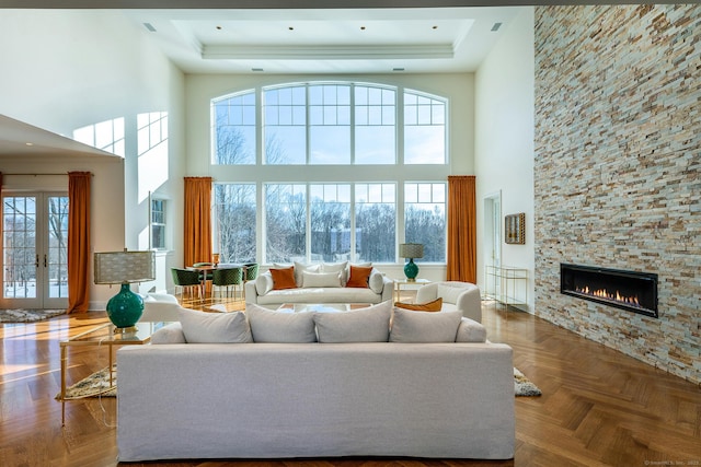 living room with a stone fireplace, a raised ceiling, and a towering ceiling