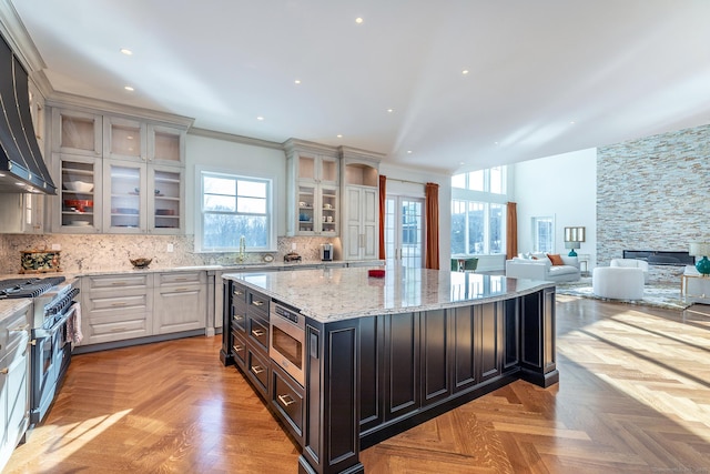 kitchen with a kitchen island, glass insert cabinets, light stone counters, backsplash, and stainless steel appliances