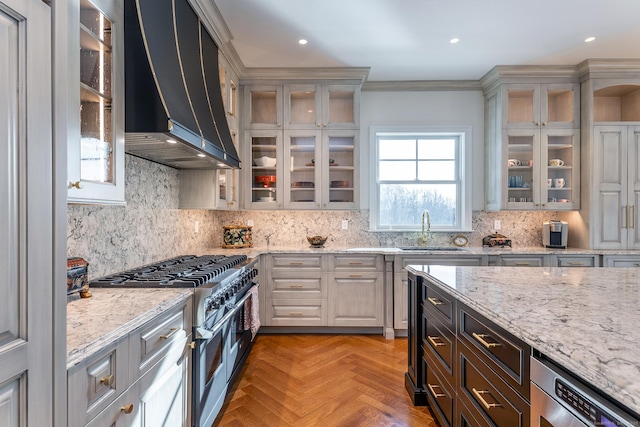 kitchen with decorative backsplash, double oven range, light stone countertops, a sink, and wall chimney exhaust hood