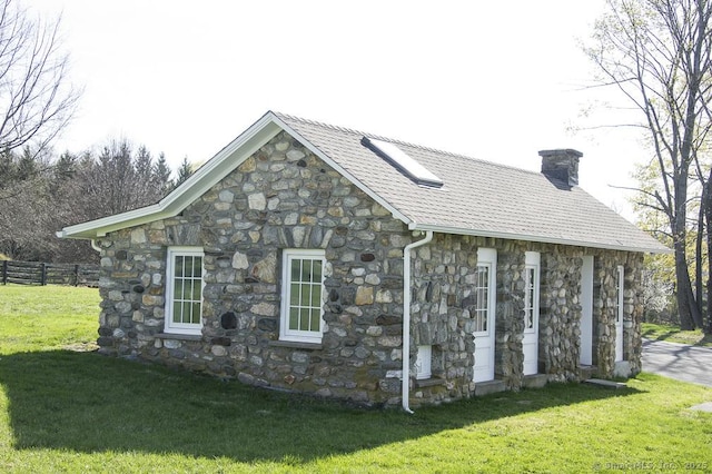 view of side of home featuring a chimney, fence, a yard, and stone siding