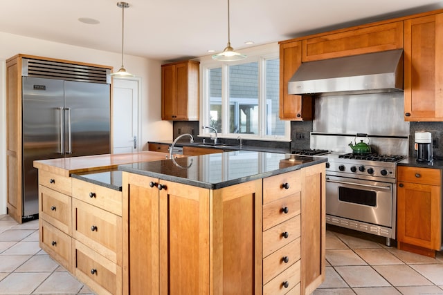 kitchen featuring sink, hanging light fixtures, premium appliances, an island with sink, and wall chimney exhaust hood