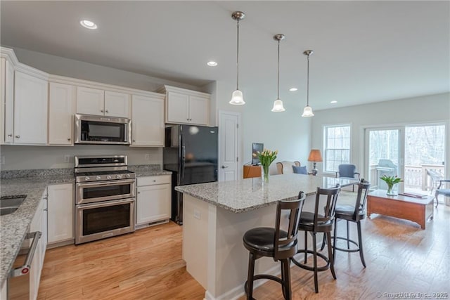 kitchen featuring a breakfast bar, stainless steel appliances, light hardwood / wood-style floors, white cabinets, and a kitchen island