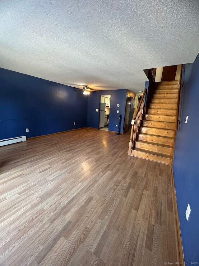 unfurnished living room with hardwood / wood-style floors, baseboard heating, and a textured ceiling