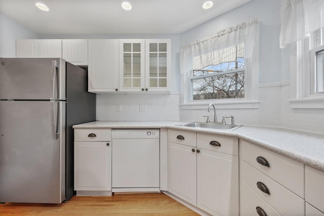 kitchen with sink, stainless steel refrigerator, white dishwasher, and white cabinetry