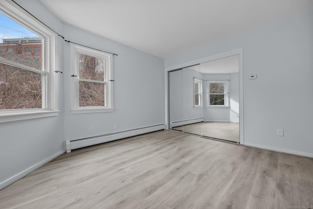 unfurnished bedroom featuring a baseboard heating unit, a closet, and light wood-type flooring