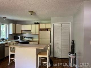 kitchen featuring a textured ceiling, dishwasher, a kitchen island, range with electric stovetop, and a breakfast bar