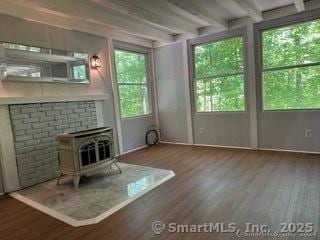 unfurnished living room with a wood stove, dark hardwood / wood-style floors, beamed ceiling, and a healthy amount of sunlight