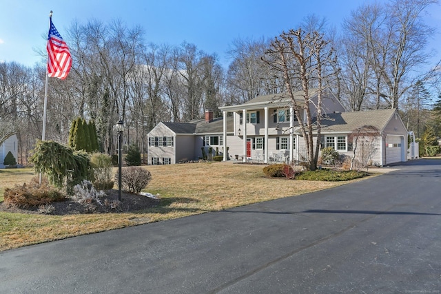 greek revival inspired property featuring covered porch, aphalt driveway, a front yard, and a garage