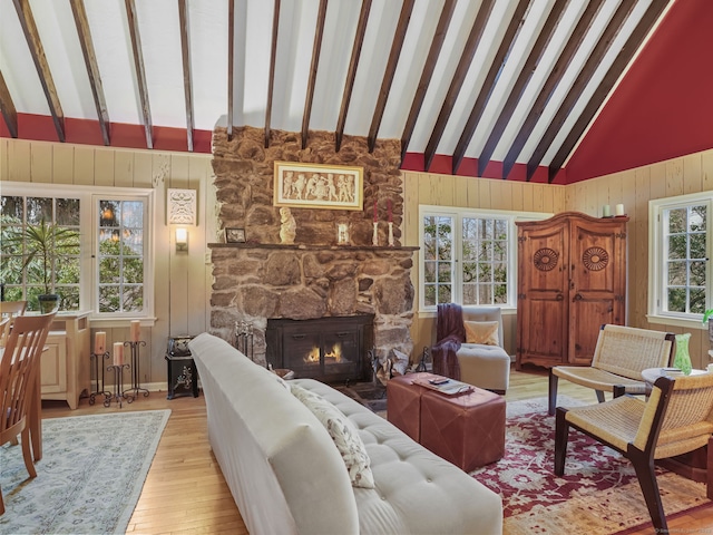 living room with light hardwood / wood-style flooring, beam ceiling, wooden walls, high vaulted ceiling, and a fireplace