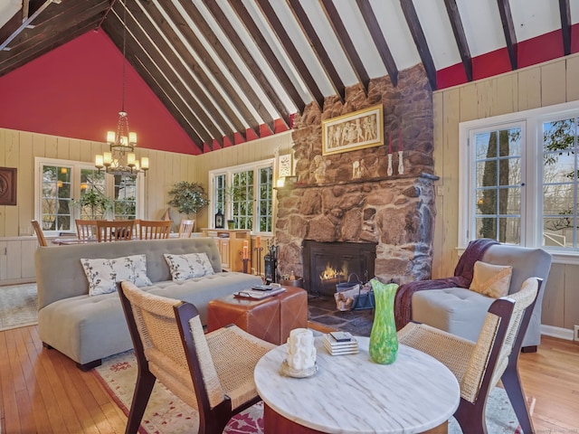 dining space with a stone fireplace, a chandelier, high vaulted ceiling, beam ceiling, and hardwood / wood-style floors