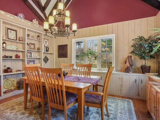 dining room with vaulted ceiling, hardwood / wood-style floors, a chandelier, and wood walls